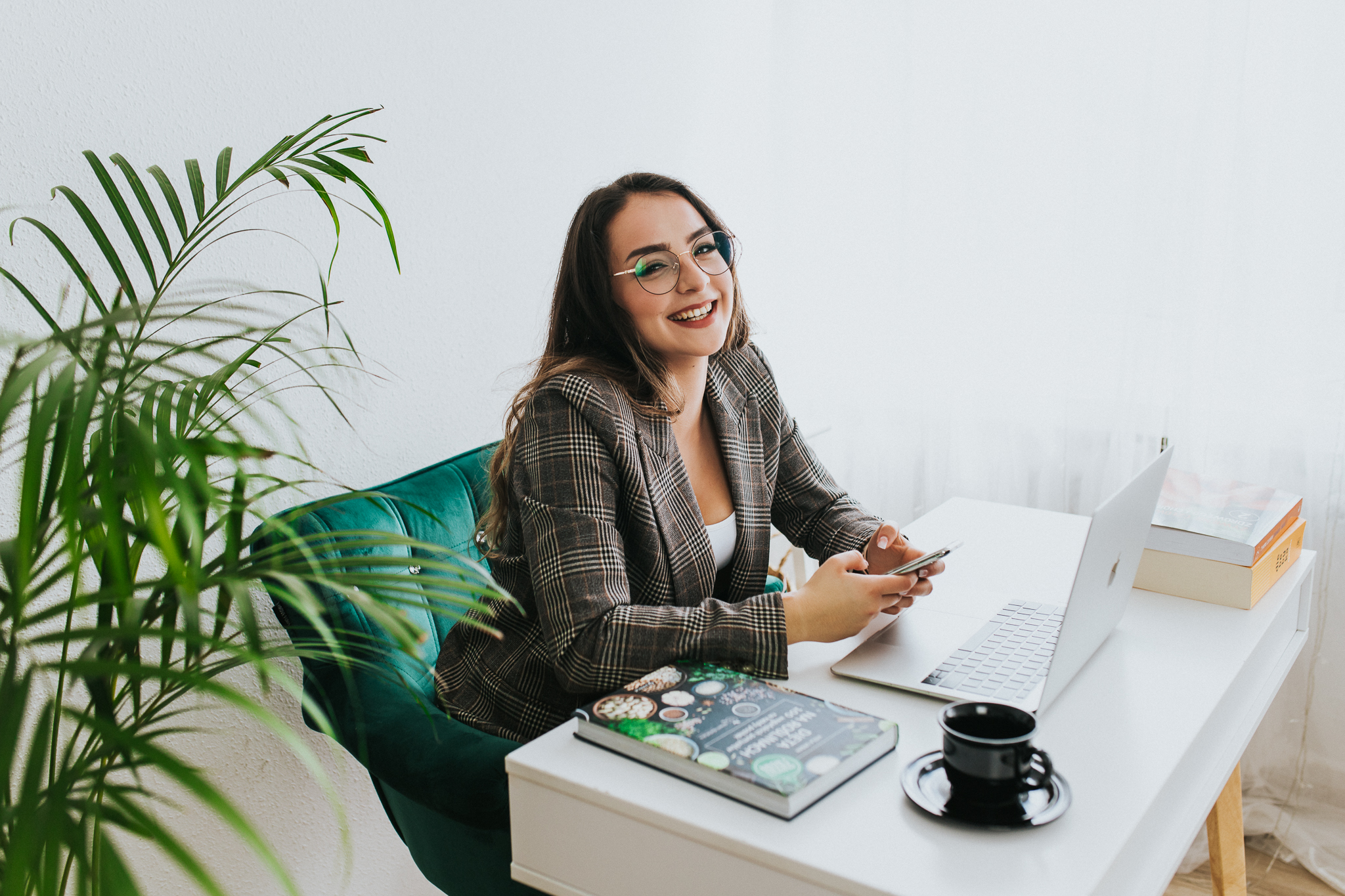 Uśmiechnięta kobieta prowadząca rozmowę przy biurku na którym stoi czarna fliżanka i książki