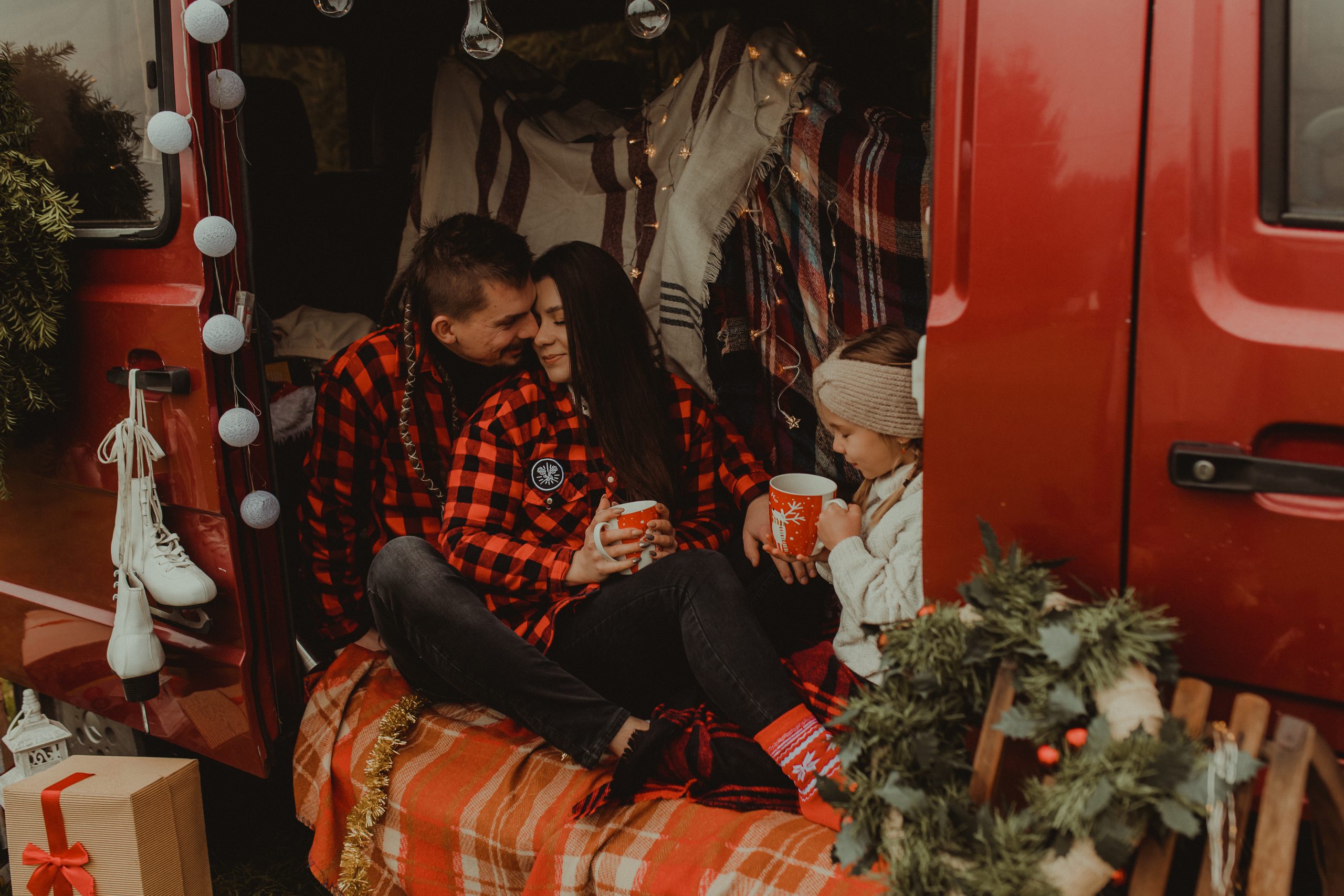 Wnętrze samochodu w kocach w środku siedzi kobieta i mężczyzna oraz dziecko, wszyscy trzymają czerwone kubki
