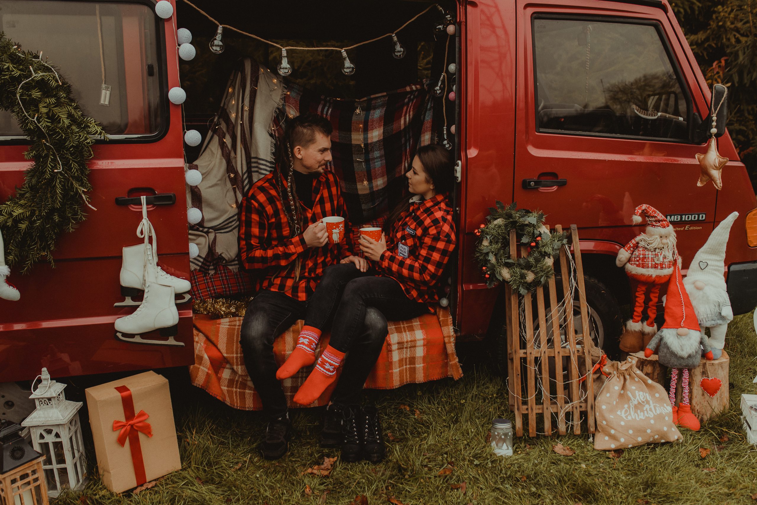 Kobieta i mężyczna siedzą w busie. W rękach trzymają czerwone, świąteczne kubki. Sesja świąteczna