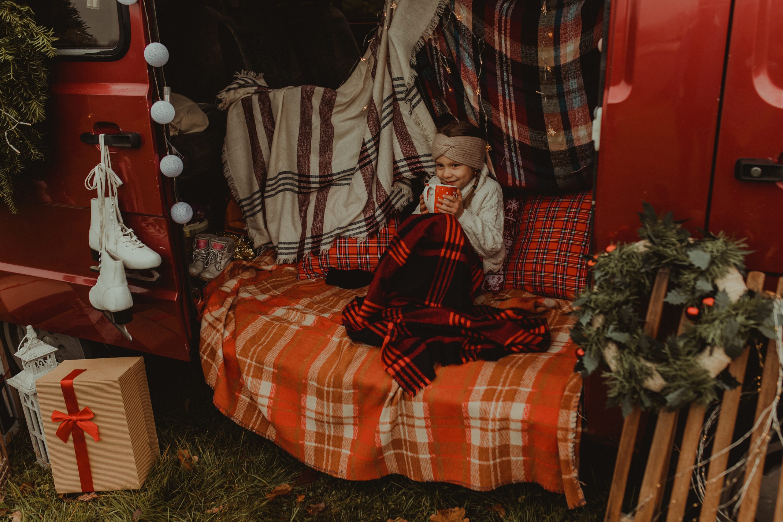 Dziewczynka wtulona w koc. W rękach trzyma czerwony kubek.