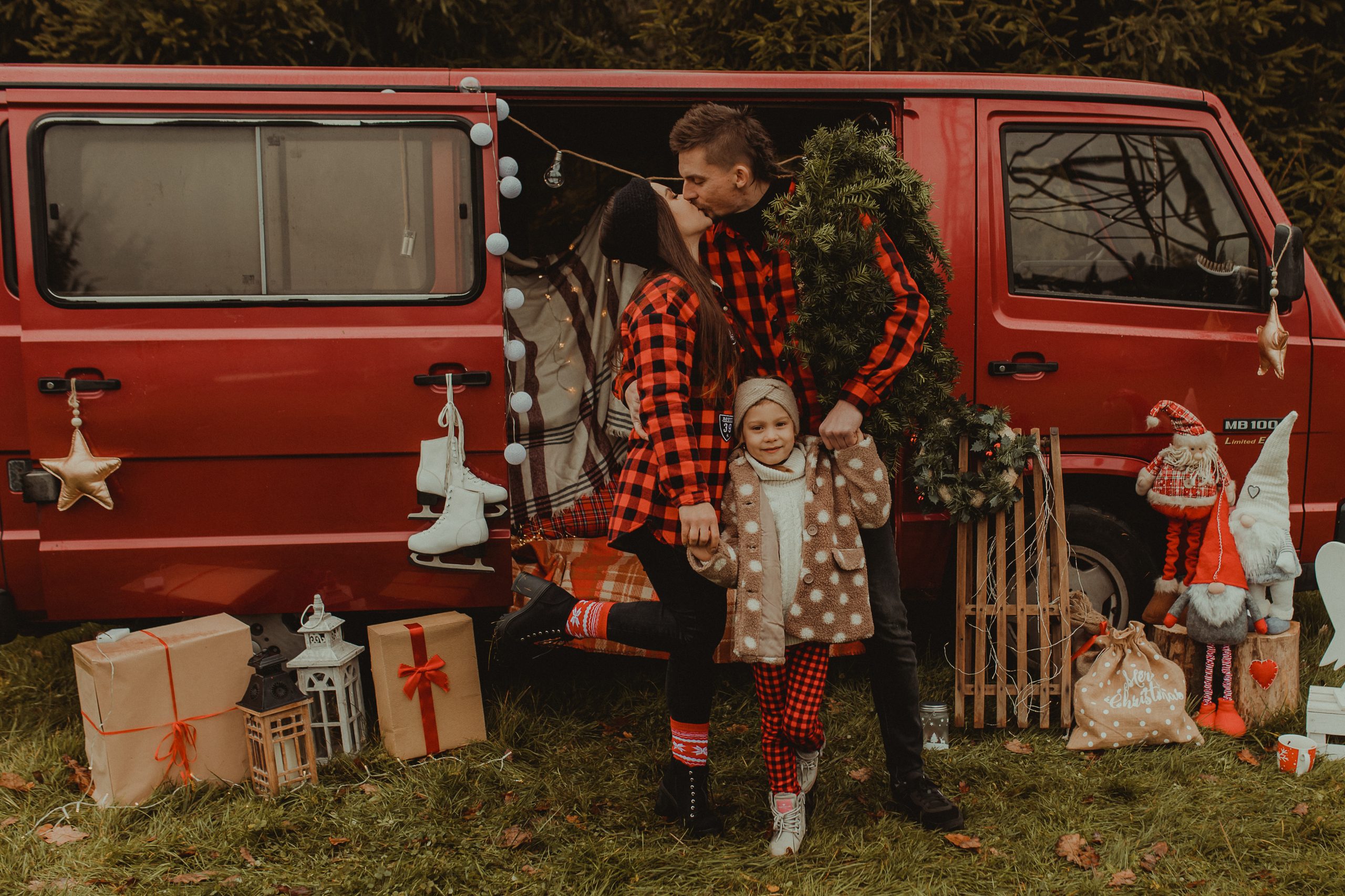 Kobieta całuje mężczyznę przed busem. Mężczyzna ma na ramieniu świąteczny wieniec, trzymają za ręce dziecko