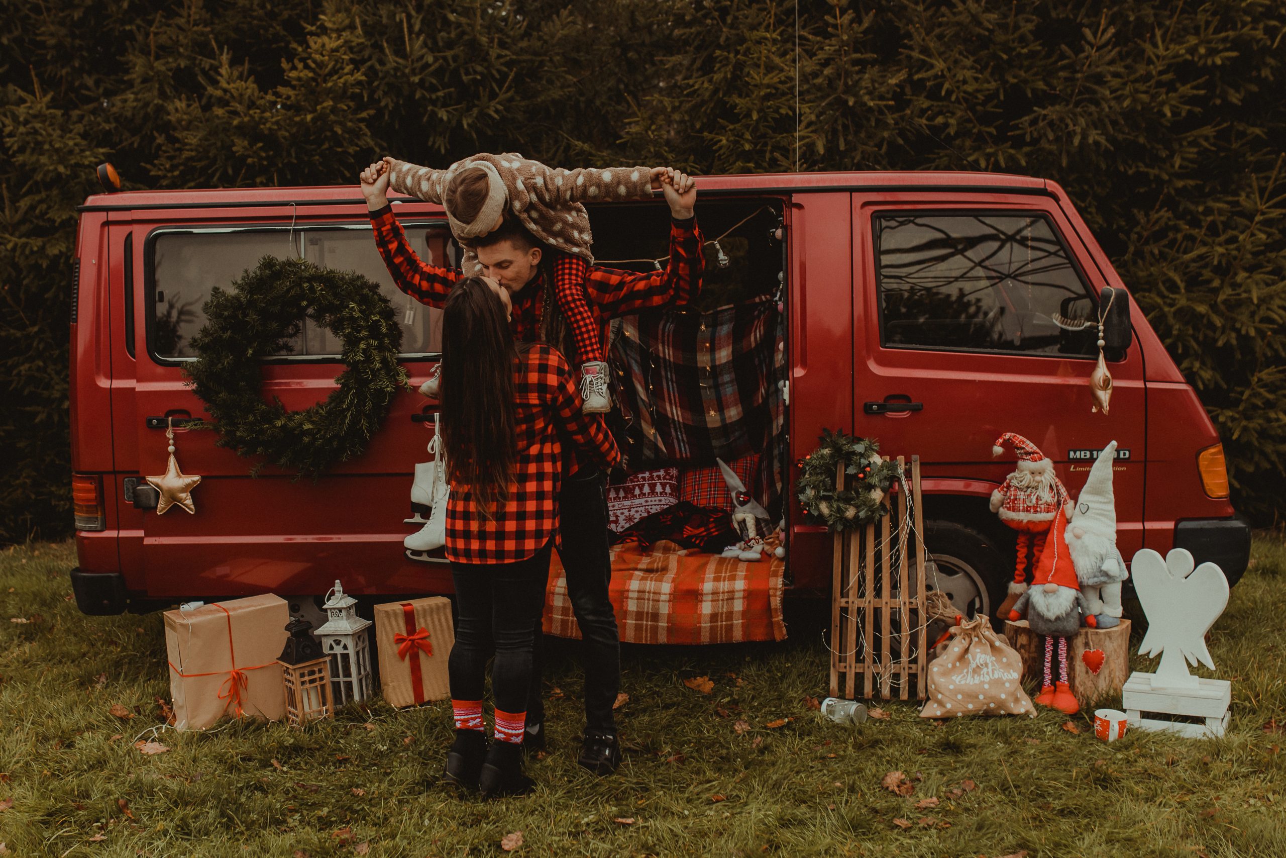 Ojciec trzyma córkę na barana i całuje mamę. Wszystko dzieje się przed świątecznym busem