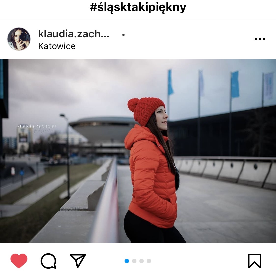 Dziewczyna w czerwonej kurtce i czapce stoi na chodniku. W tle katowicki Spodek. #śląsktakipiękny