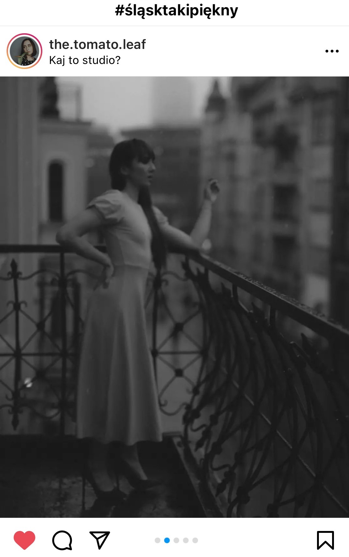 Kobieta w sukience na balkonie. Rękę opartą ma o poręcz.