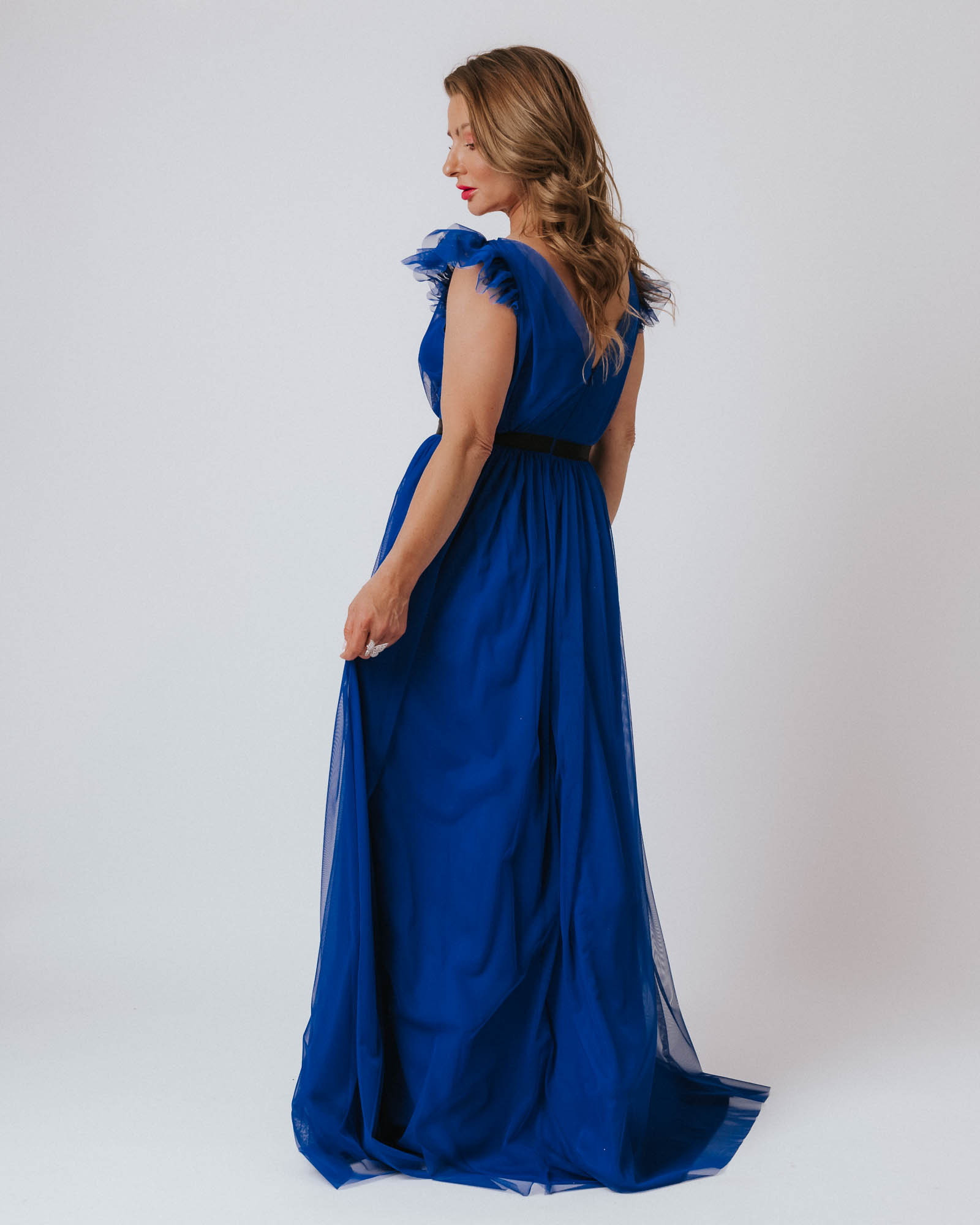 Kobieta w niebieskiej sukni odwrócona tyłem spogląda w bok