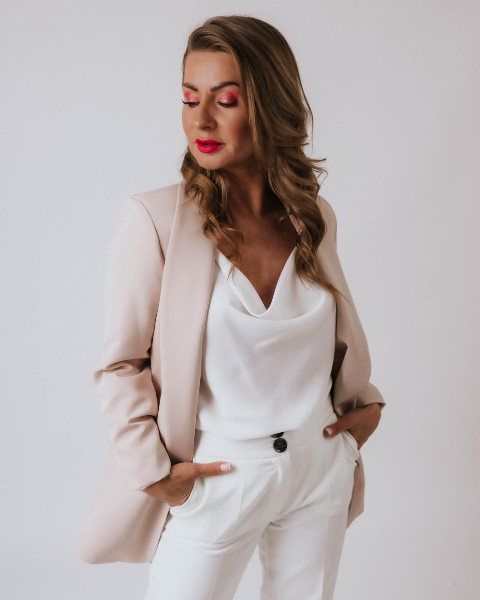 Kobieta w beżowej marynarce trzymająca ręce w kieszeni