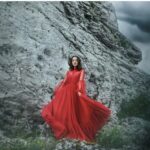 kobieta w balowej, czerwonej sukni na tle skały w tle czarne chmury