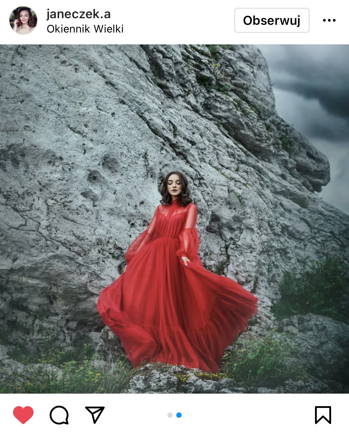 kobieta w balowej, czerwonej sukni na tle skały w tle czarne chmury
