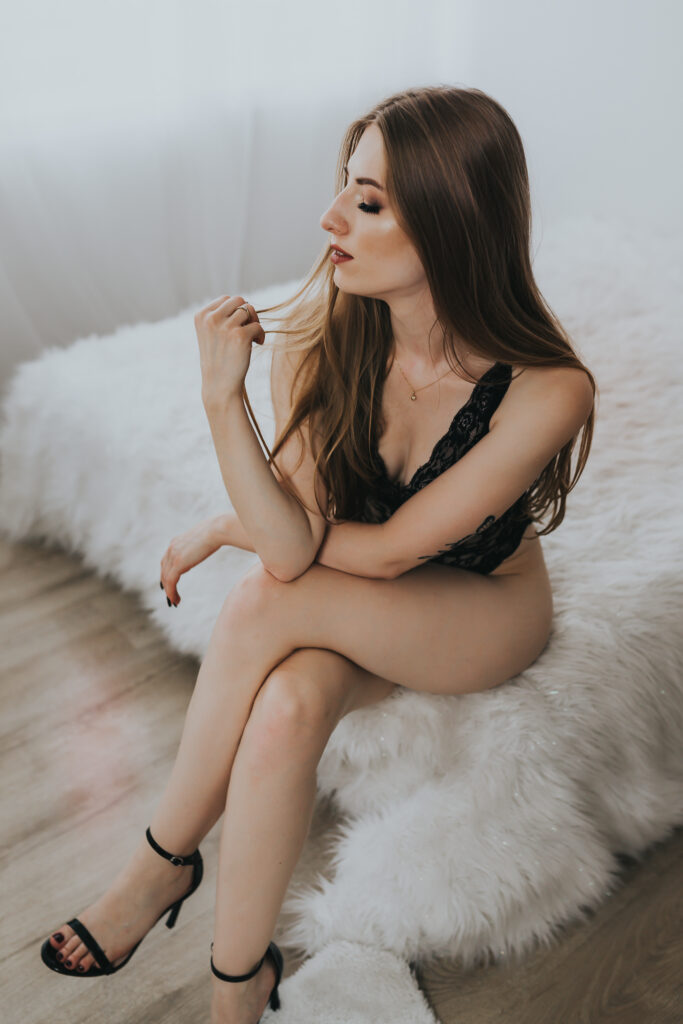 kobieta w body, siedzi na krawędzi łóżka zamyślona i bawi się włosami