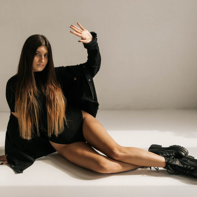 Kobieta siedzi na podłodze i ma lewą rękę uniesioną do góry