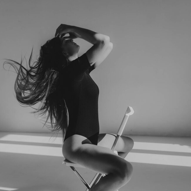 Kobieta siedząca na krześle, rękę trzyma na twarzy ma rozkudlone włosy. Zdjęcie czarno- białe