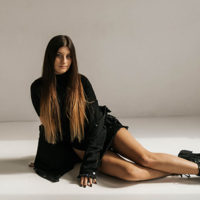 Kobieta ubrana na czarno z gołymi nogami siedzi na podłodze, Fusialka