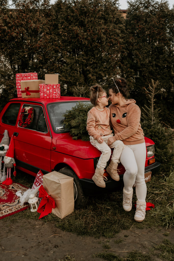 matka z córką siedzą na masce czerwonego samochodu i patrzą sobie w oczy