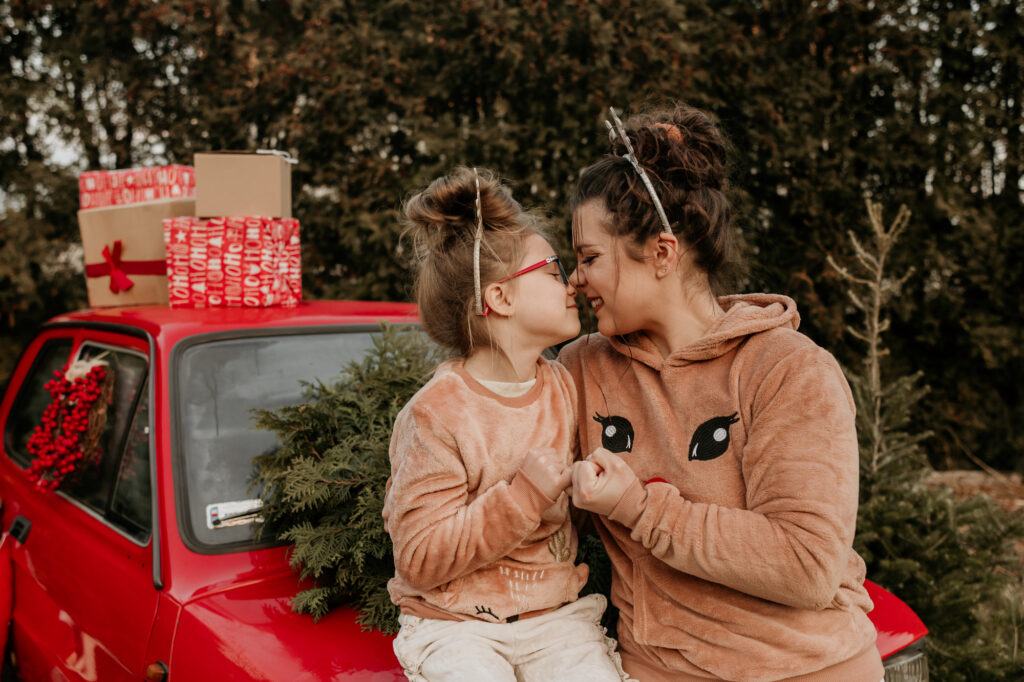 matka z córką tulą się nosami i dają sobie żółwika na masce samochodu