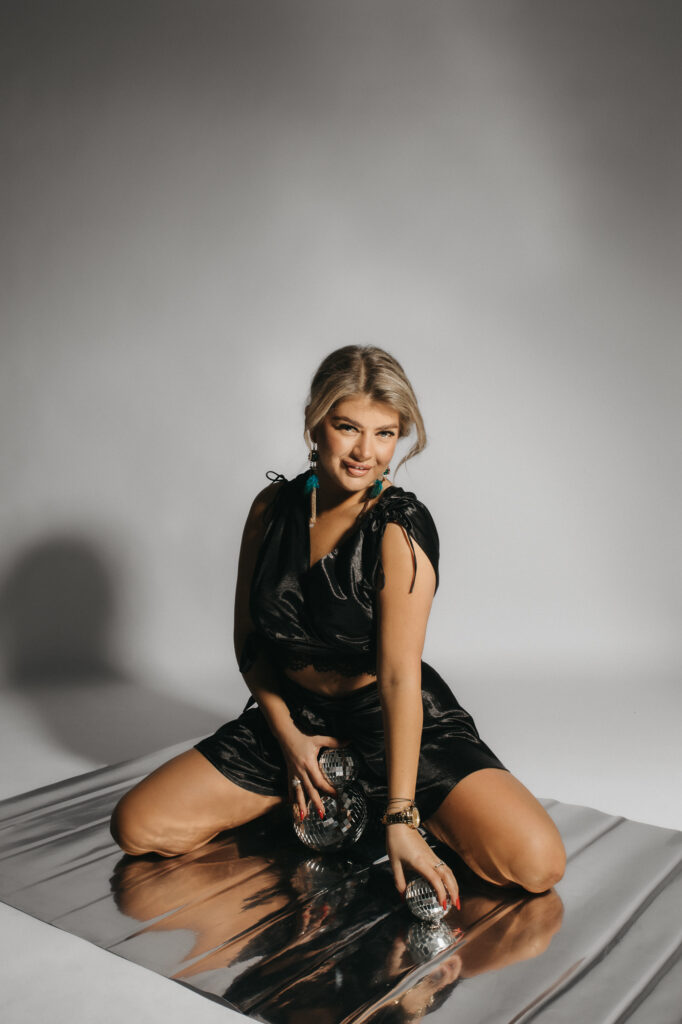 kobieta siedzi na folii w rękach trzyma srebrną kulę, jest elegancko ubrana