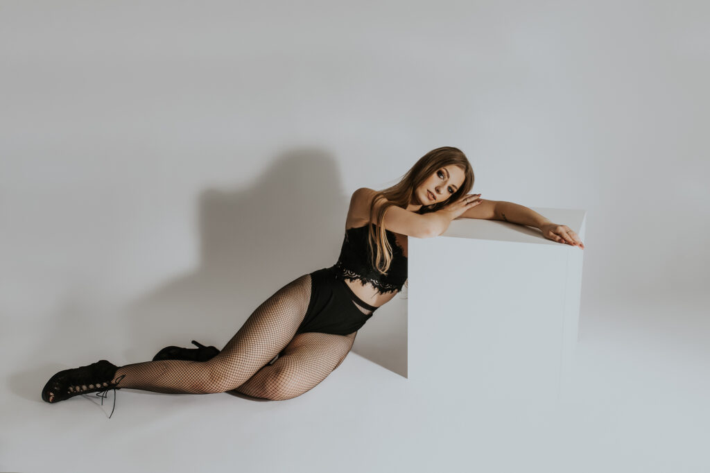 Młoda, szczupła kobieta leży oparta o podest jest ubrana w czarny stanik i czarne rajstopy