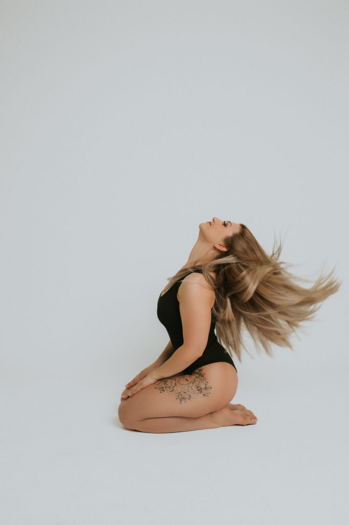 kobieta klęczy bokiem do obiektywu, ma rozdmuchane włosy