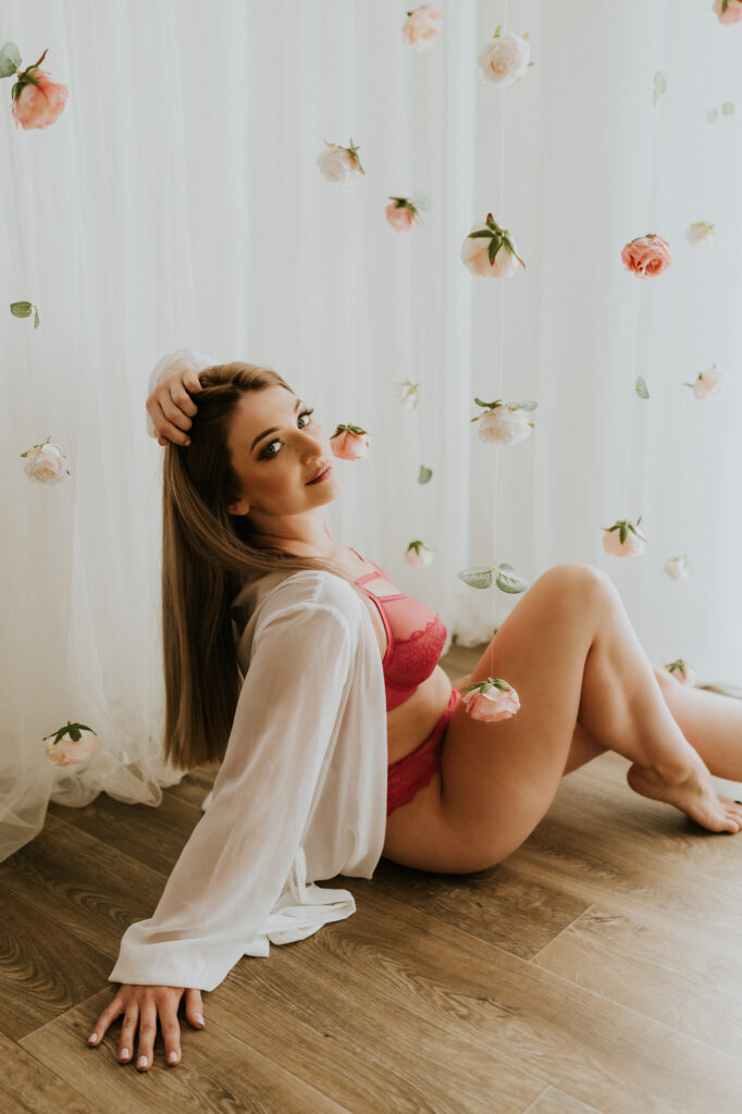 kobieta siedzi w kwiatach, ma ubraną białą narzutkę