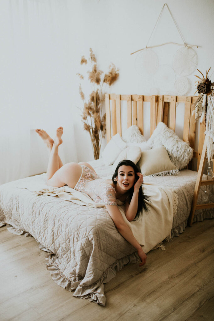 Kobieta leży na łóżku i pozuje. Ubrana jest w body.