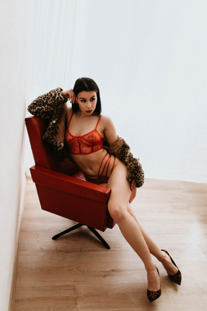 Kobieta w czerwonej bieliźnie i futrze siedzi na krześle