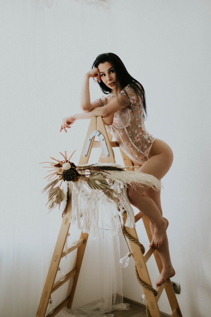 Brunetka stoi na drabinie i pozuje, ubrana jest w body.