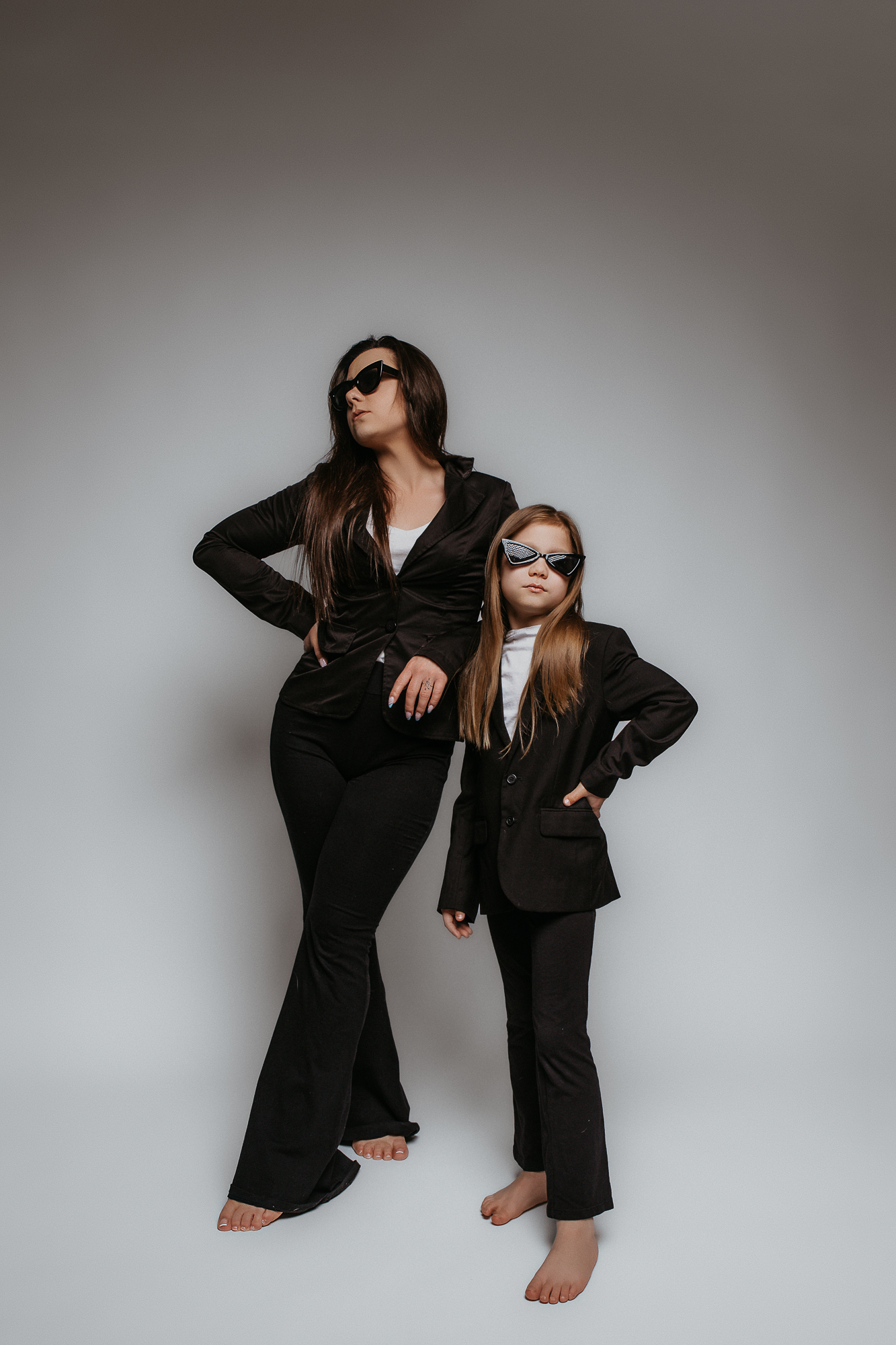 matka i córka stoją tak samo ubrane w czarne garnitury i czanr okulary