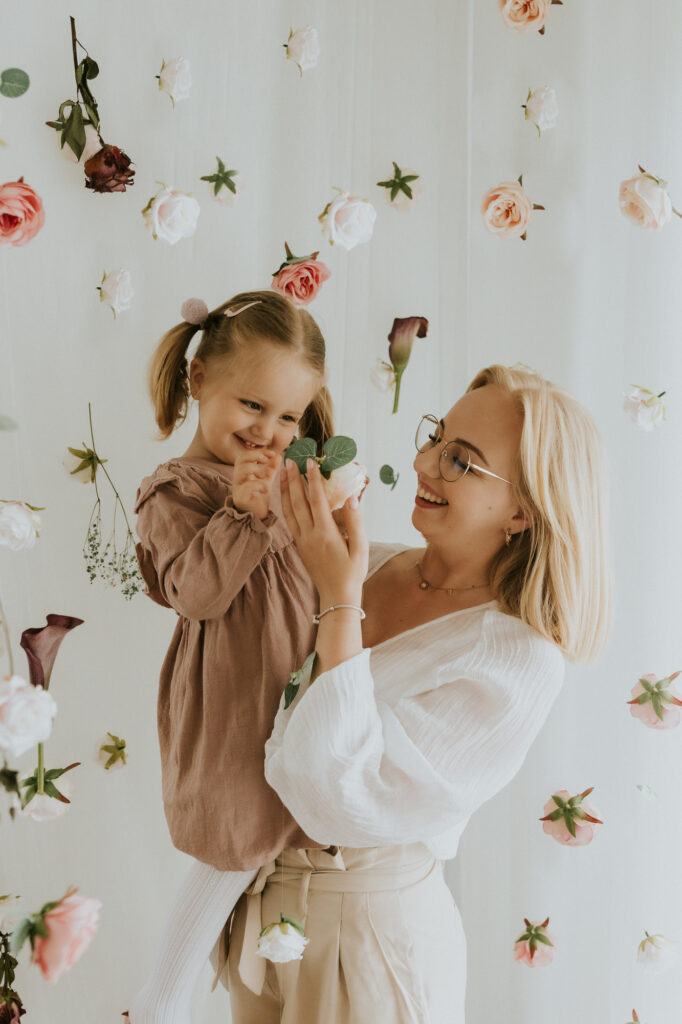 kobieta trzyma dziewczynkę na rękach dookoła pełno kwiatów