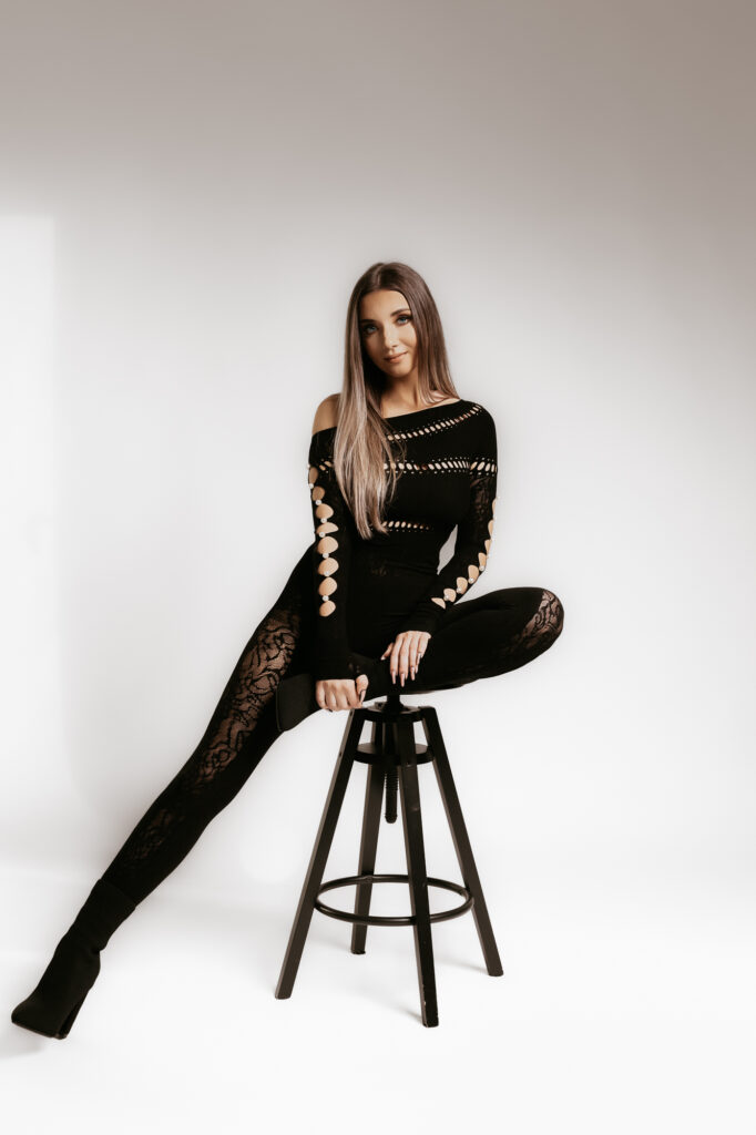 kobieta ubrana w czarny kombinezon pozuje na krześle