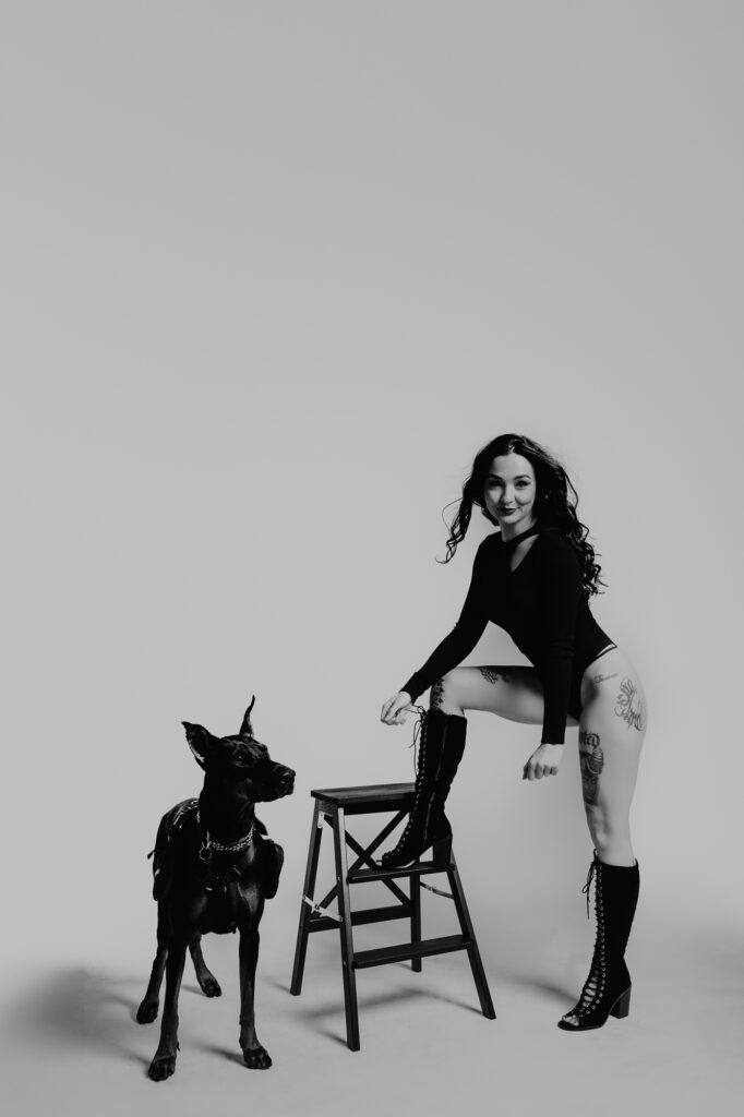 kobieta na krześle ubrana na czarno z dobermanem
